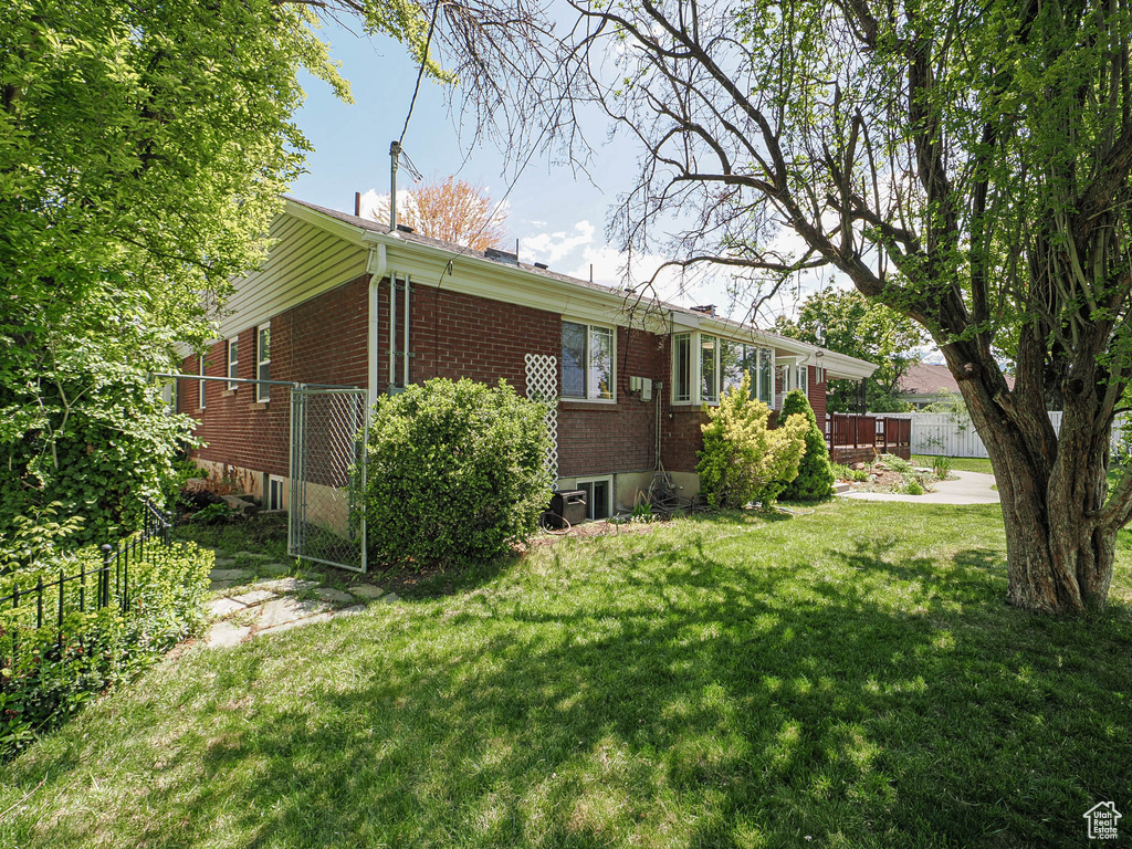 View of home's exterior featuring fence, a lawn, a deck, and brick siding