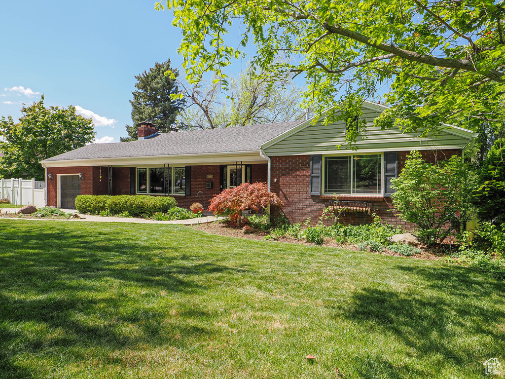 Ranch-style home with fence, a front lawn, brick siding, a garage, and a chimney