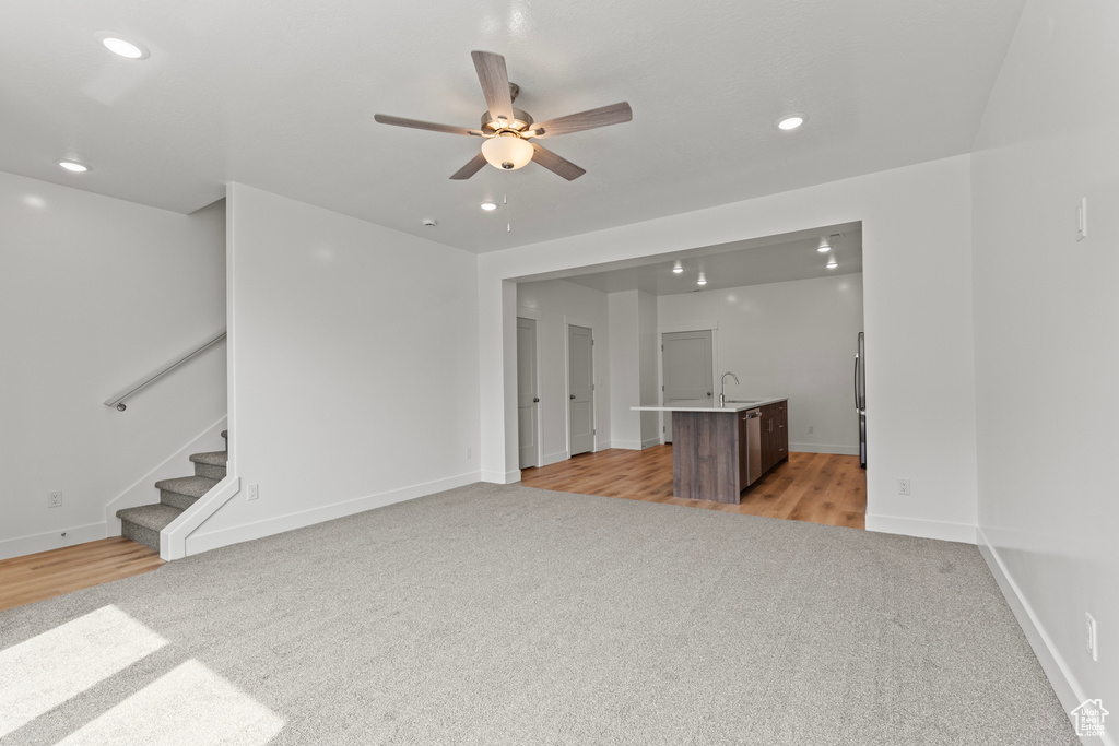 Unfurnished living room with light colored carpet, a ceiling fan, stairs, and recessed lighting