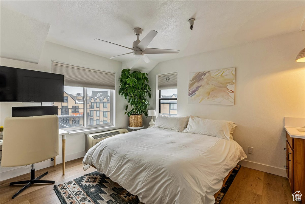 Bedroom featuring baseboards, a textured ceiling, a wall unit AC, and wood finished floors