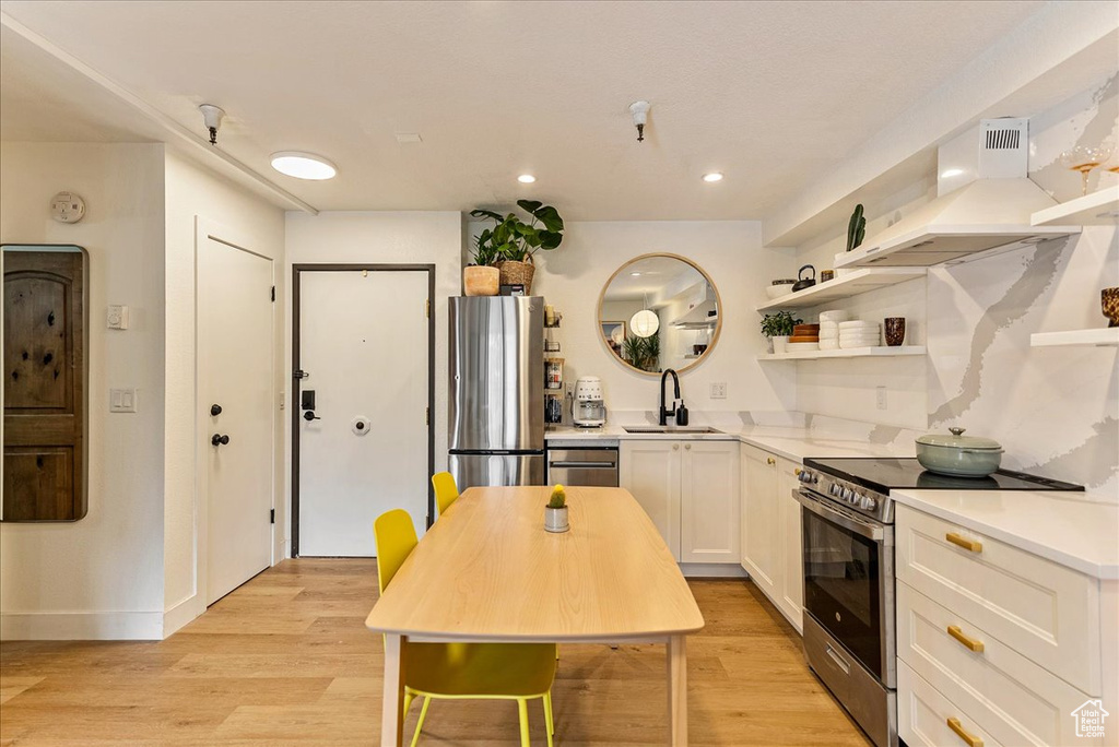 Kitchen featuring open shelves, light wood-type flooring, custom range hood, a sink, and stainless steel appliances