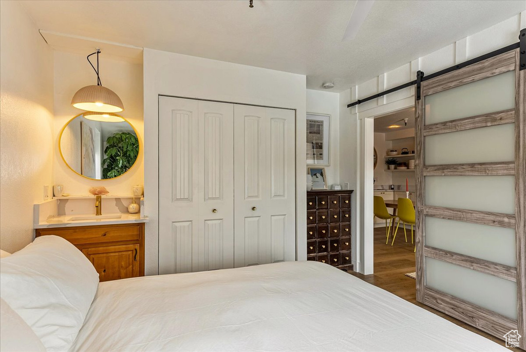 Bedroom with a closet, wood finished floors, ensuite bathroom, a barn door, and a sink