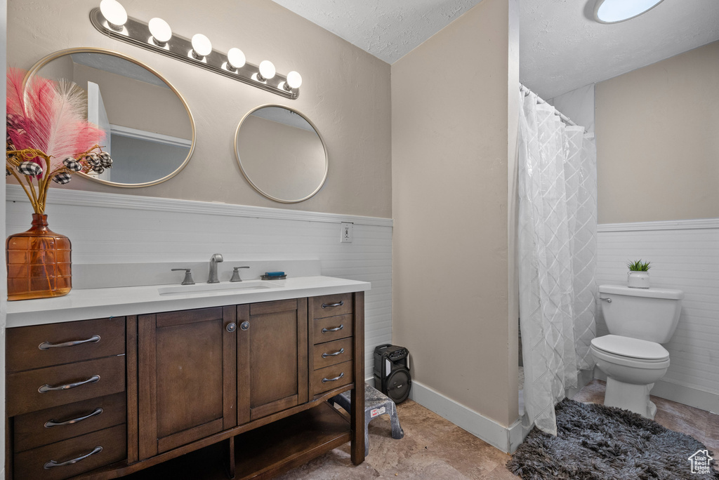 Full bathroom with vanity, curtained shower, toilet, a textured ceiling, and a wainscoted wall