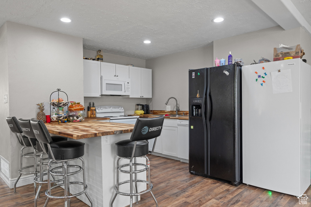 Kitchen featuring white appliances, wooden counters, white cabinetry, a peninsula, and a kitchen bar