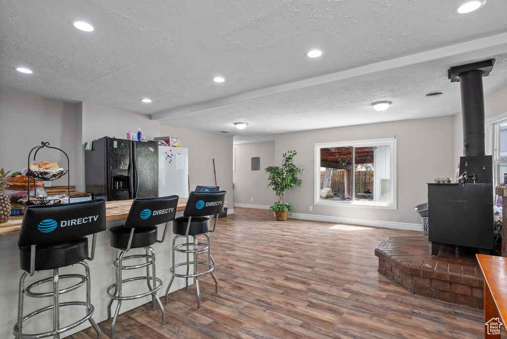 Kitchen featuring black fridge with ice dispenser, a wood stove, a textured ceiling, and wood finished floors