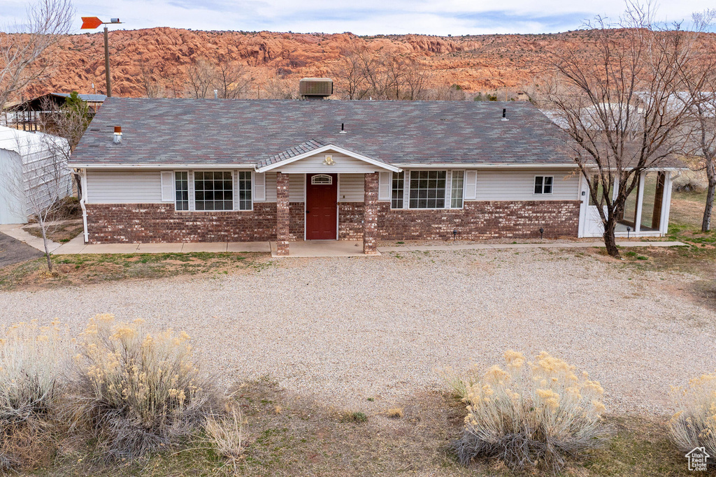 Ranch-style home featuring a mountain view, central air condition unit, a shingled roof, and brick siding