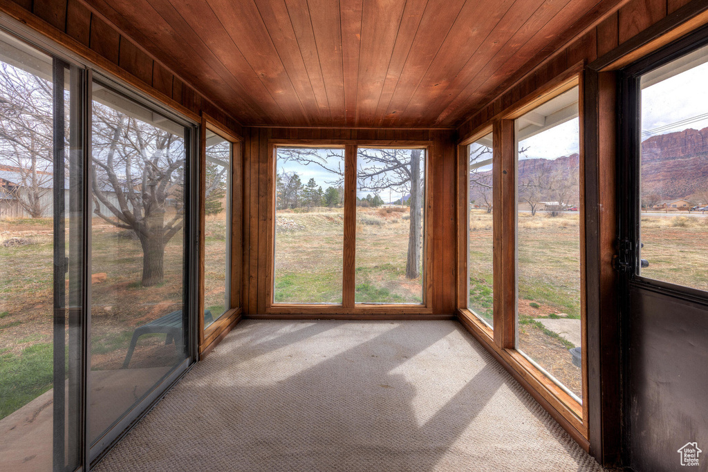 Unfurnished sunroom featuring a mountain view, wooden ceiling, and carpet floors