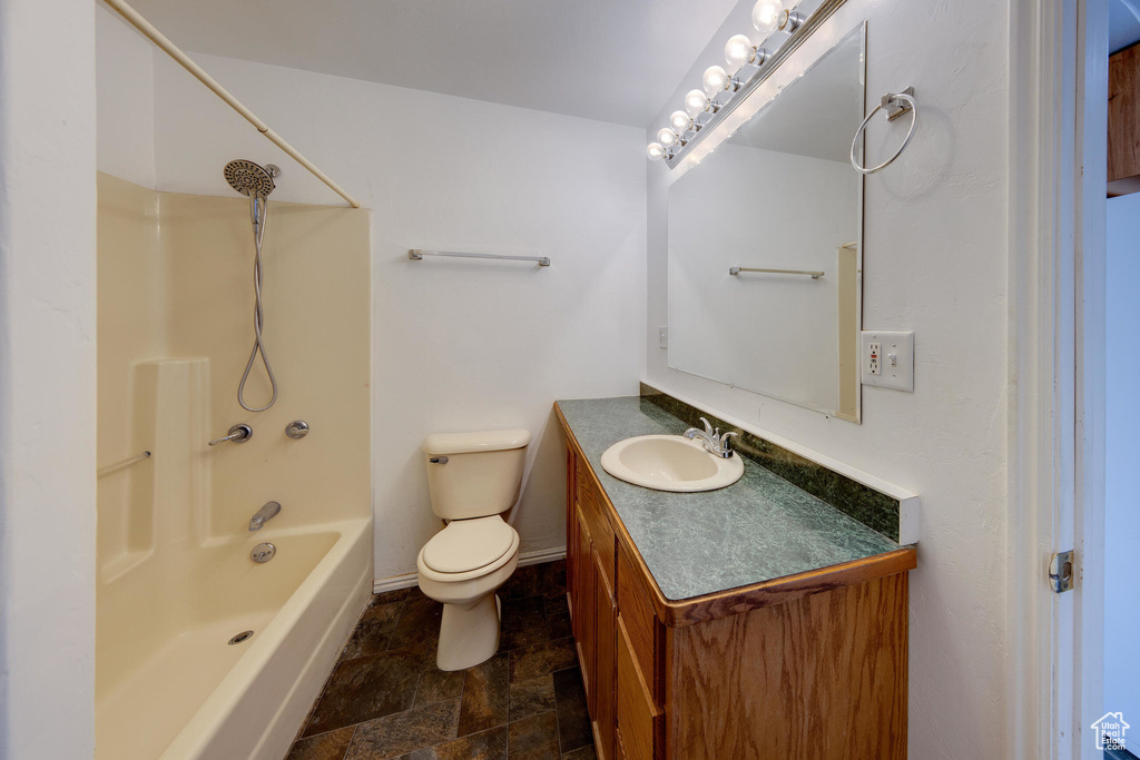 Full bath featuring vanity, bathing tub / shower combination, toilet, stone finish floor, and baseboards
