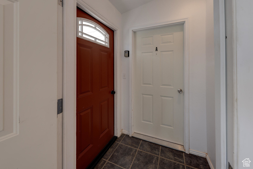 Doorway with dark tile patterned floors and baseboards