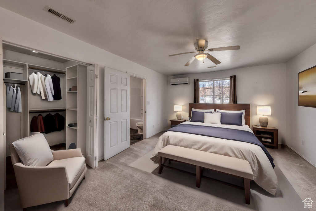 Carpeted bedroom with connected bathroom, ceiling fan, visible vents, a closet, and an AC wall unit