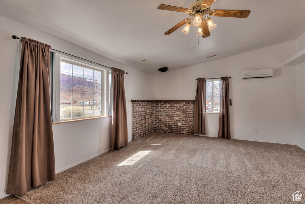 Carpeted empty room with vaulted ceiling, a wall unit AC, a ceiling fan, and baseboards