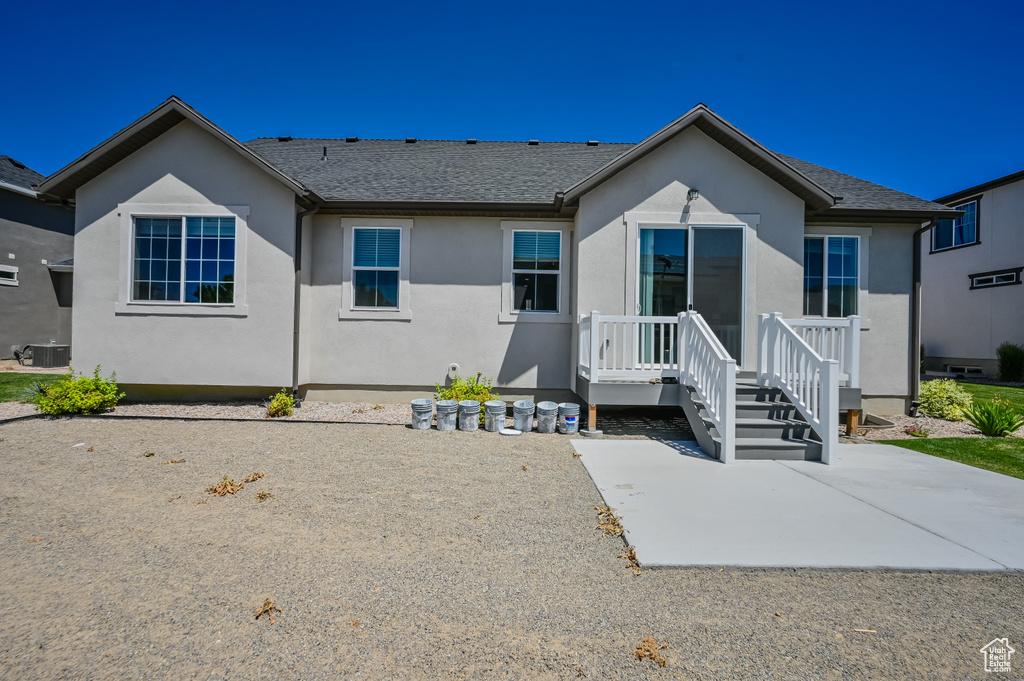 View of front facade with central AC, a shingled roof, stucco siding, and a patio
