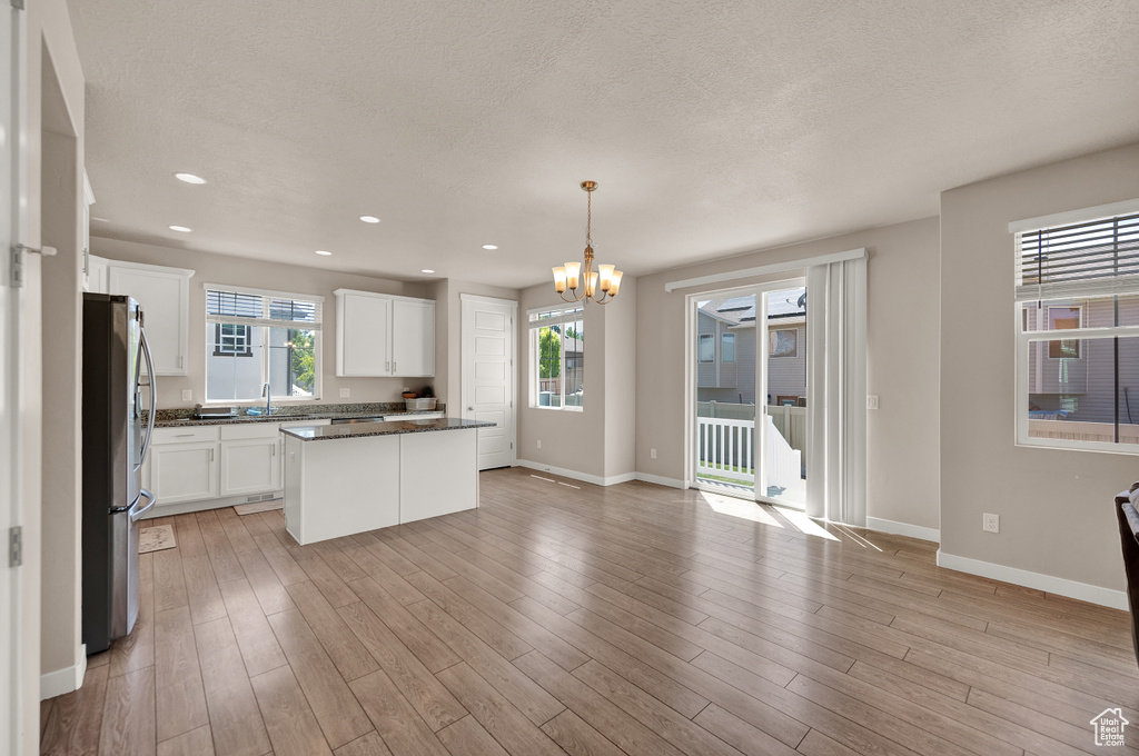 Kitchen featuring a notable chandelier, a textured ceiling, freestanding refrigerator, white cabinetry, and baseboards