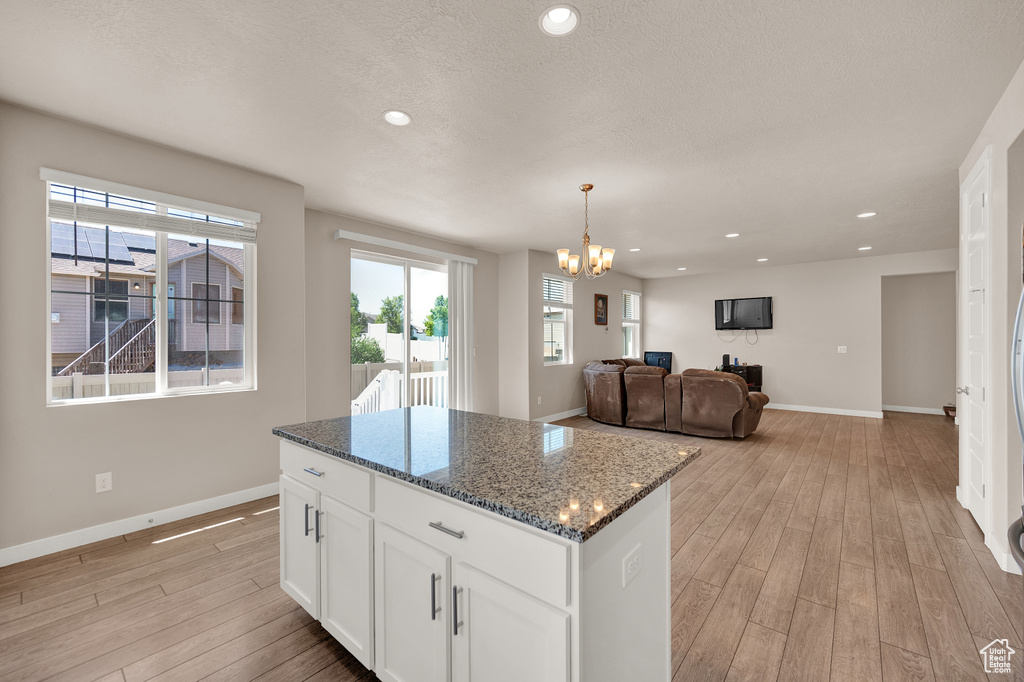 Kitchen with a kitchen island, light wood-type flooring, baseboards, a chandelier, and dark stone counters