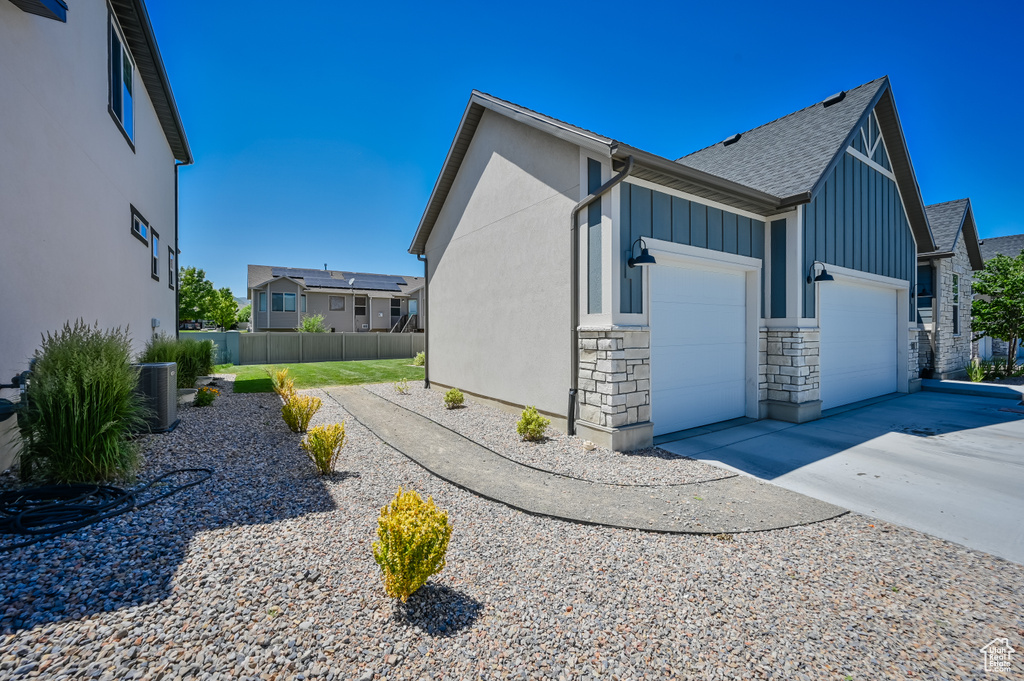 View of side of home featuring roof with shingles, fence, an attached garage, board and batten siding, and driveway