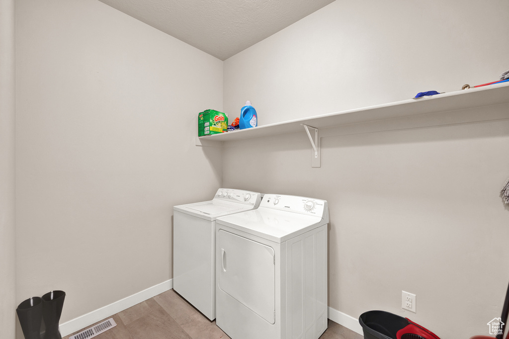 Clothes washing area featuring laundry area, independent washer and dryer, visible vents, baseboards, and light wood-style floors