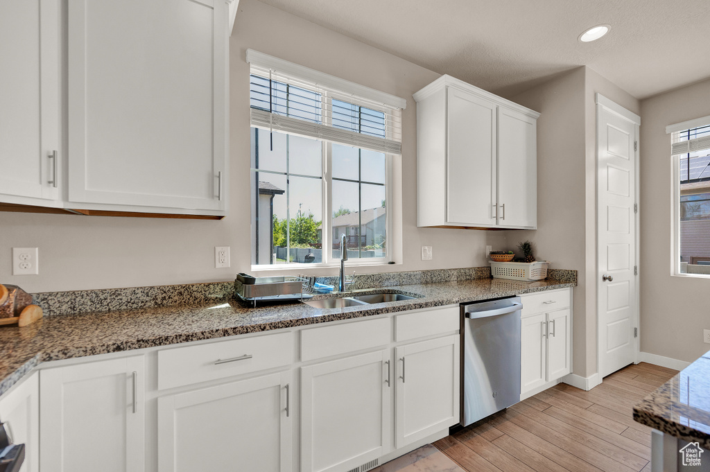 Kitchen with stainless steel dishwasher, a sink, stone countertops, light wood finished floors, and white cabinetry