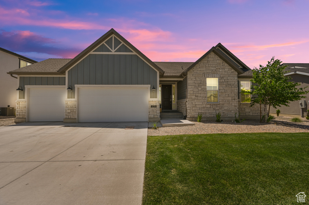 Ranch-style house featuring board and batten siding, driveway, a lawn, a garage, and stone siding
