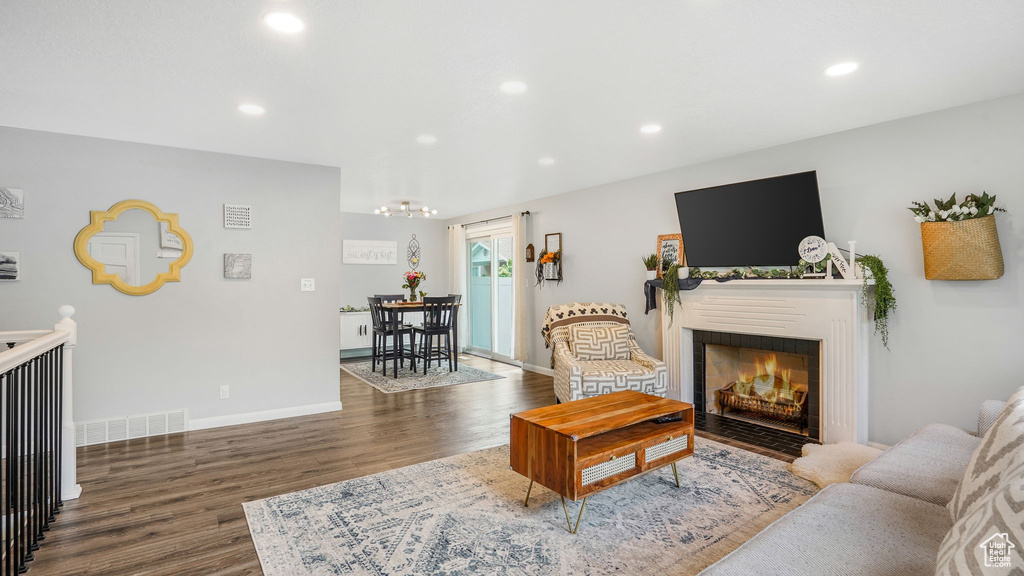 Living area with an inviting chandelier, dark wood finished floors, recessed lighting, baseboards, and a fireplace with flush hearth