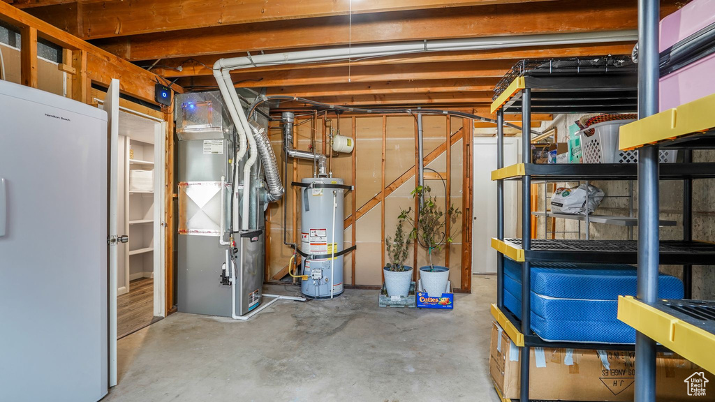 Unfinished below grade area with freestanding refrigerator, heating unit, and water heater