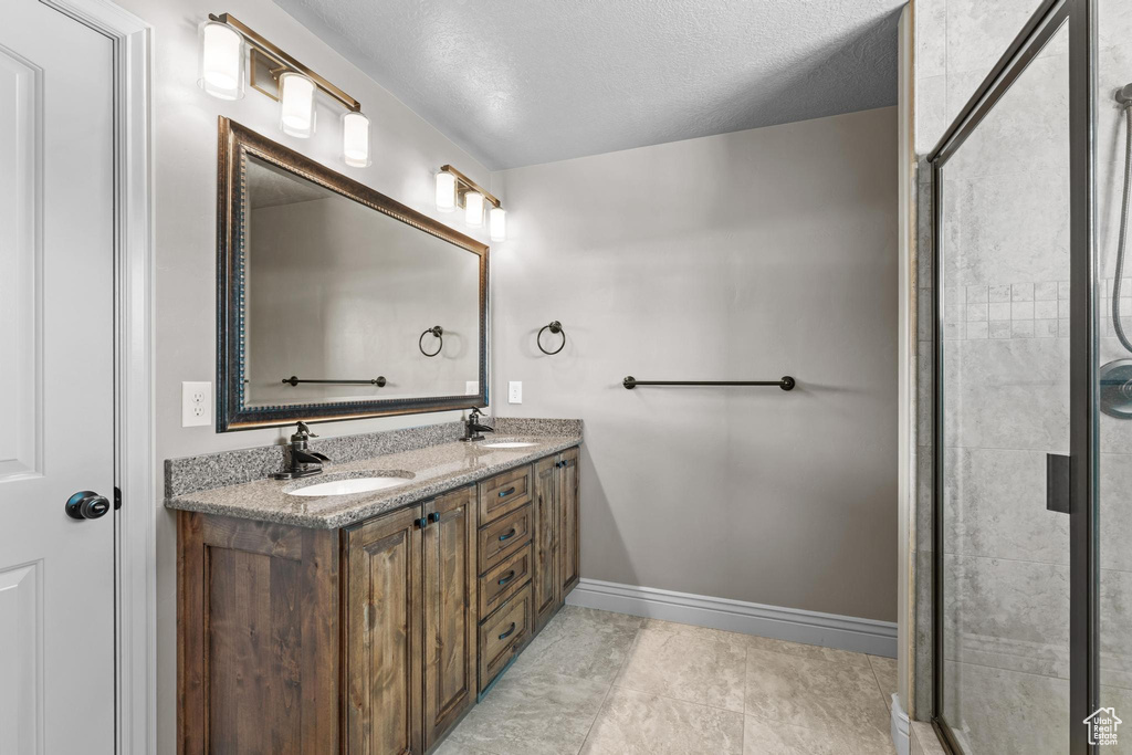 Bathroom featuring a sink, tiled shower, a textured ceiling, and double vanity