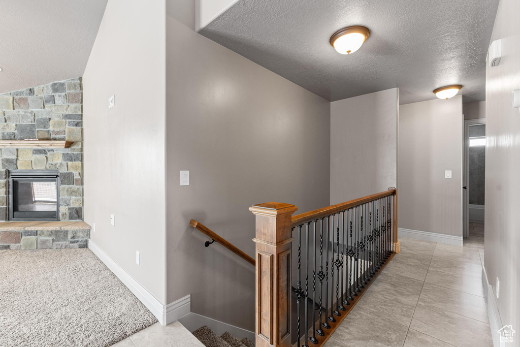 Hall featuring baseboards, a textured ceiling, tile patterned floors, and an upstairs landing