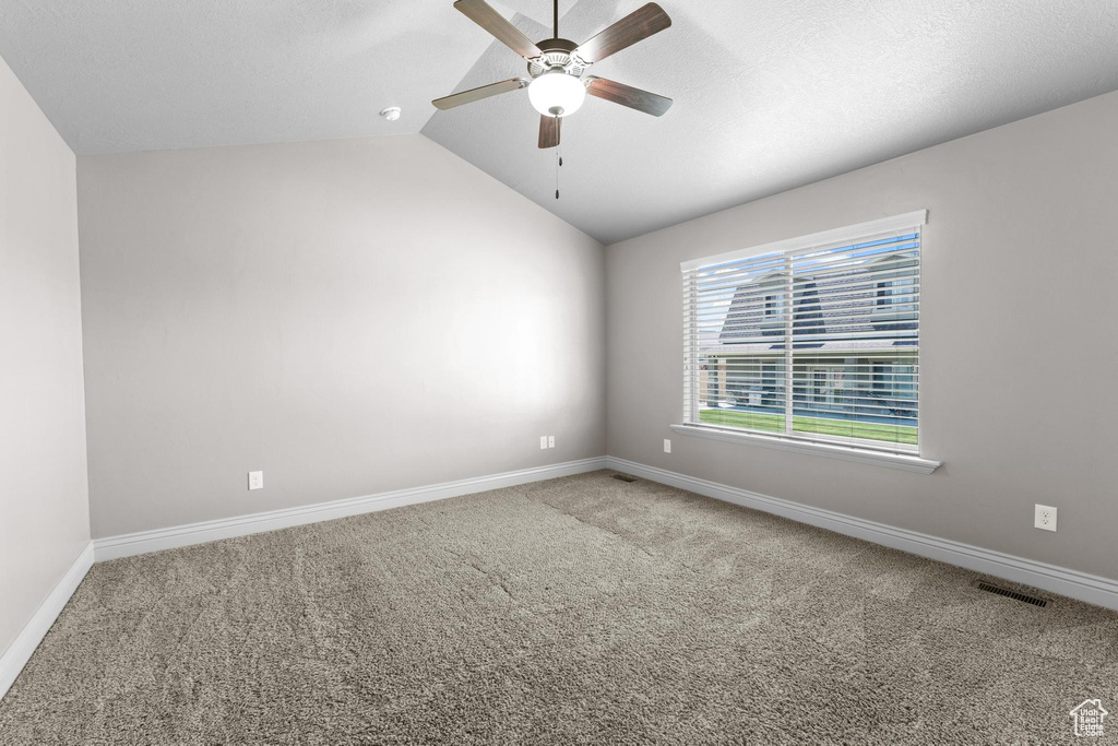 Carpeted empty room featuring vaulted ceiling, baseboards, a ceiling fan, and visible vents