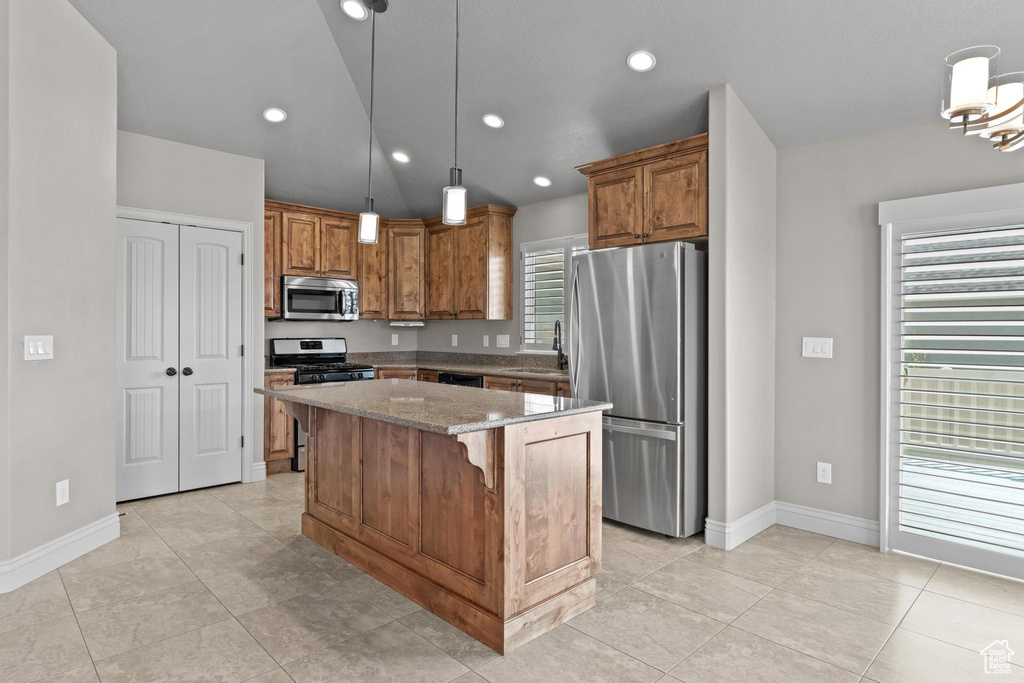 Kitchen featuring a kitchen island, appliances with stainless steel finishes, brown cabinets, baseboards, and light stone counters