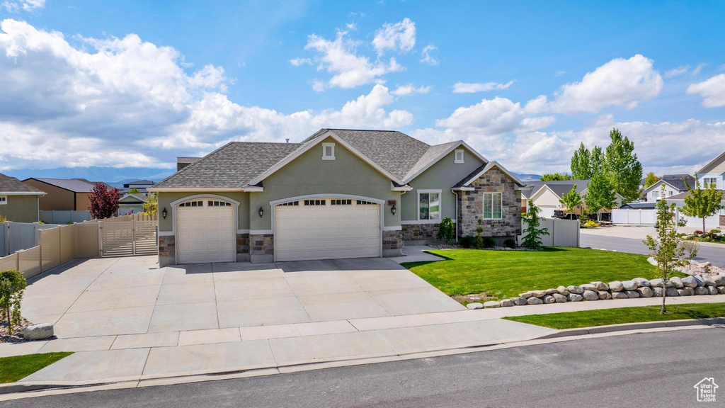 View of front of property featuring an attached garage, a front lawn, stone siding, stucco siding, and concrete driveway