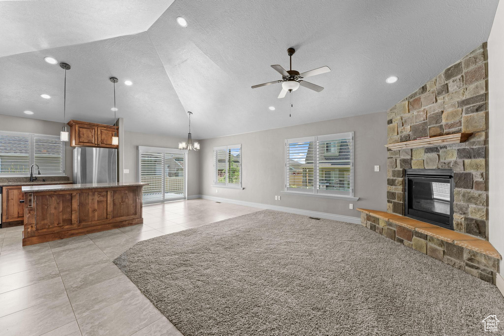Unfurnished living room featuring a textured ceiling, a stone fireplace, a sink, ceiling fan with notable chandelier, and lofted ceiling