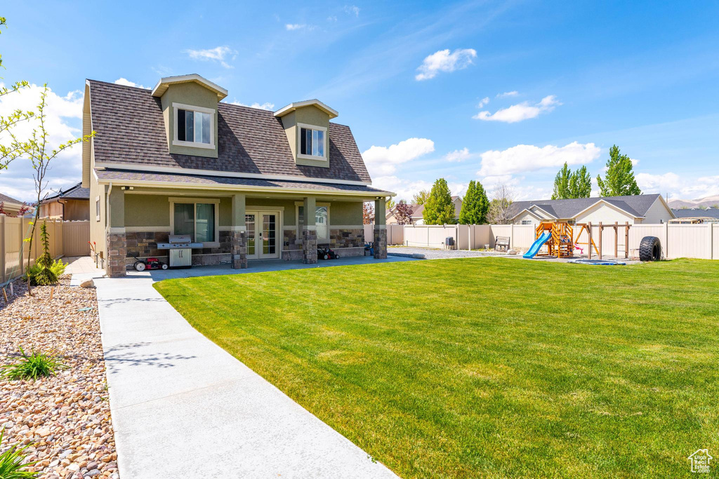 Rear view of property featuring french doors, a lawn, a playground, stone siding, and stucco siding
