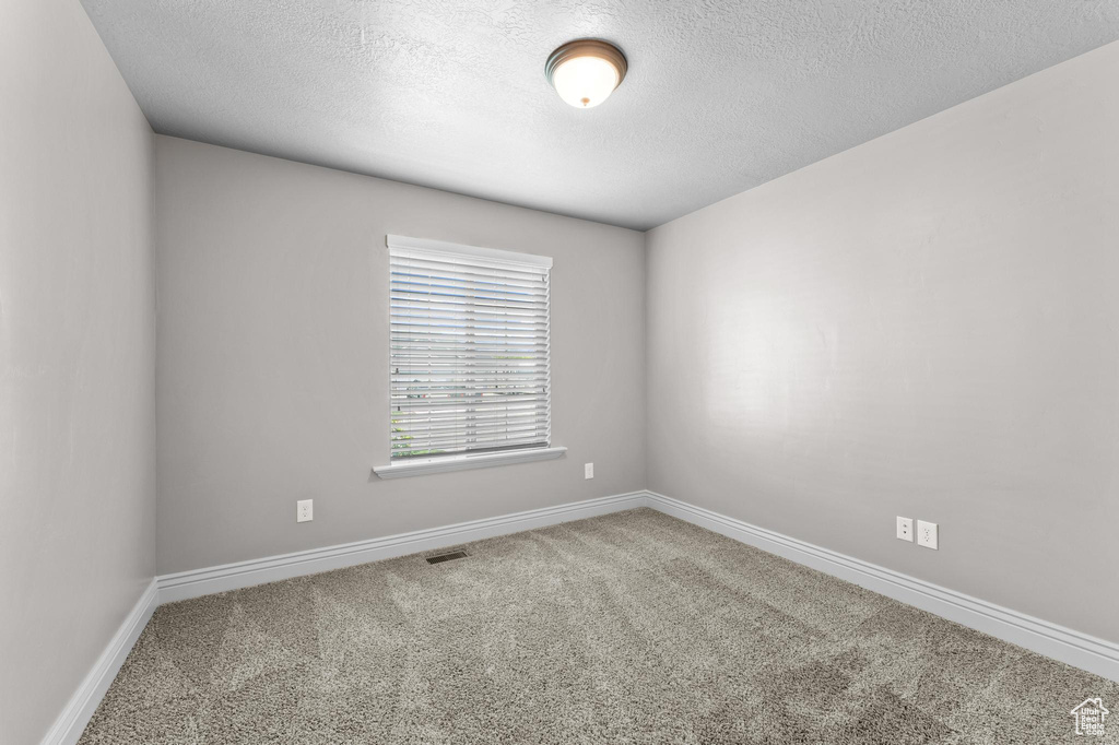 Spare room with carpet floors, a textured ceiling, visible vents, and baseboards