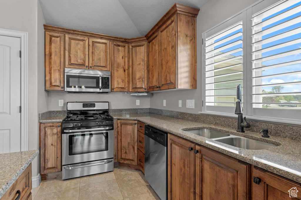 Kitchen with a sink, appliances with stainless steel finishes, brown cabinets, and light stone counters