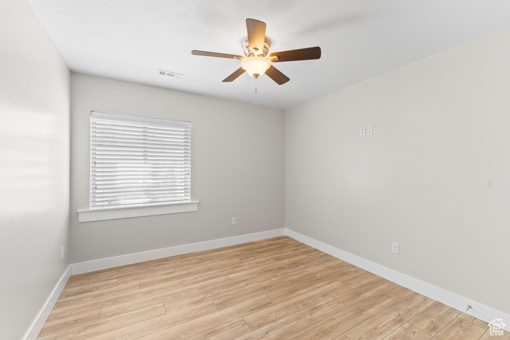 Empty room featuring light wood-style floors, baseboards, ceiling fan, and visible vents