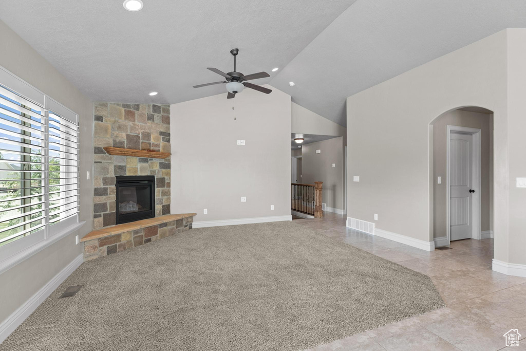 Unfurnished living room featuring arched walkways, a stone fireplace, a ceiling fan, lofted ceiling, and visible vents