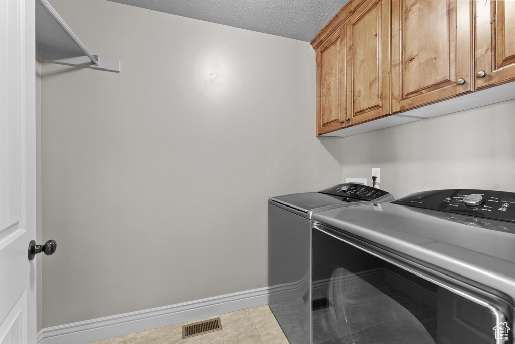 Washroom featuring a textured ceiling, visible vents, washing machine and dryer, cabinet space, and baseboards