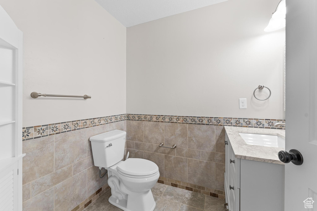 Half bathroom with vanity, wainscoting, toilet, and tile walls