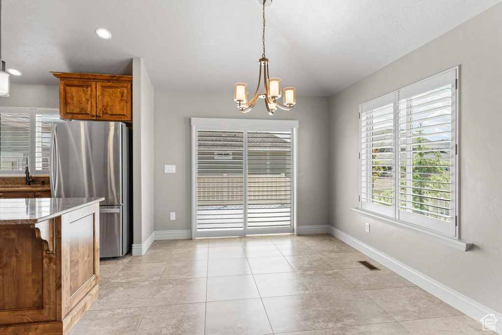 Kitchen featuring freestanding refrigerator, brown cabinets, an inviting chandelier, and a healthy amount of sunlight