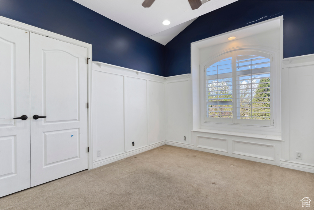 Unfurnished bedroom featuring vaulted ceiling, wainscoting, a decorative wall, and carpet flooring