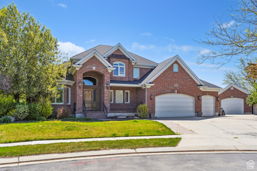 Traditional-style home with driveway, a front yard, roof with shingles, brick siding, and an attached garage