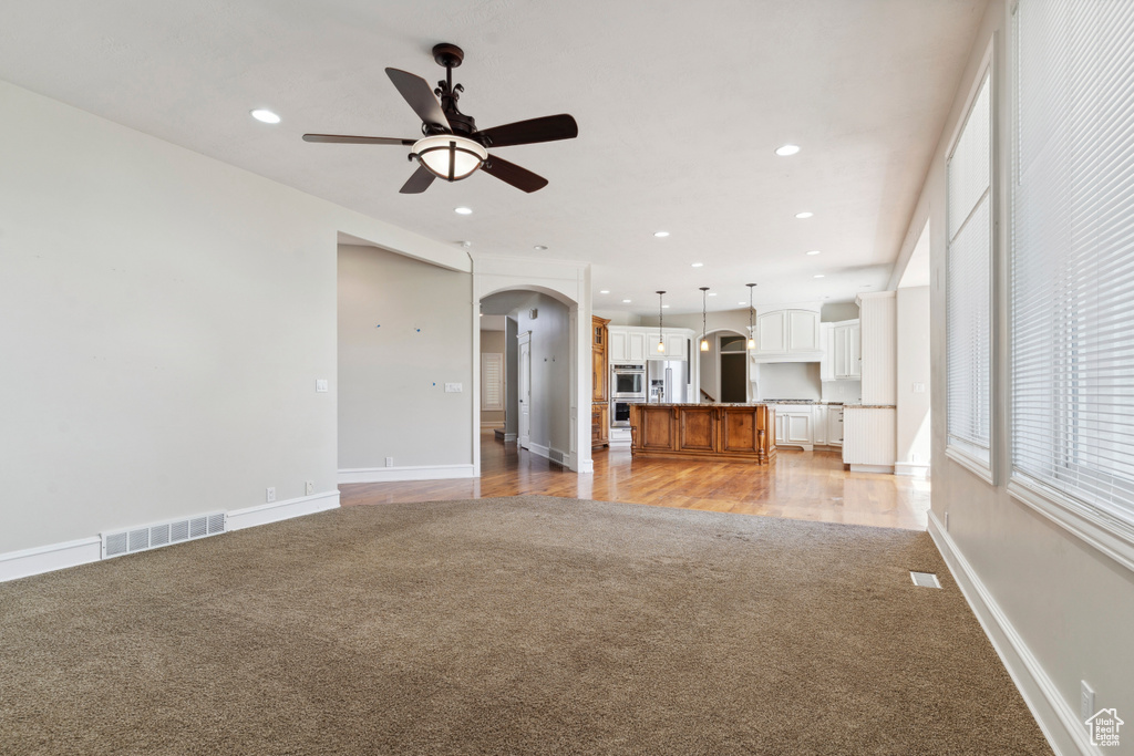 Unfurnished living room featuring ceiling fan, visible vents, light colored carpet, arched walkways, and recessed lighting
