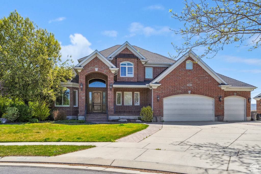 Traditional home featuring concrete driveway, brick siding, an attached garage, and a front yard