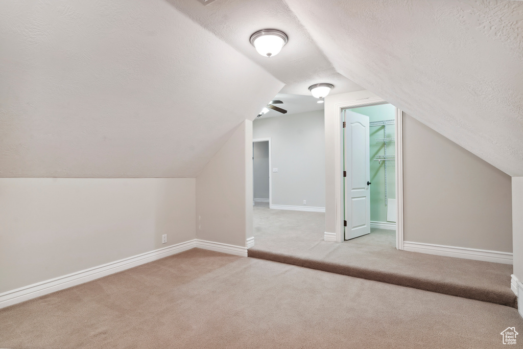 Bonus room with baseboards, a textured ceiling, lofted ceiling, and light carpet