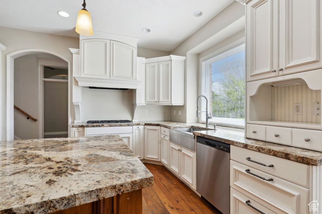Kitchen featuring appliances with stainless steel finishes, arched walkways, light stone countertops, dark wood finished floors, and a sink