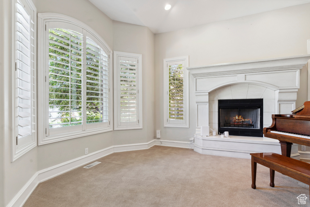 Unfurnished room featuring visible vents, vaulted ceiling, carpet floors, baseboards, and a warm lit fireplace