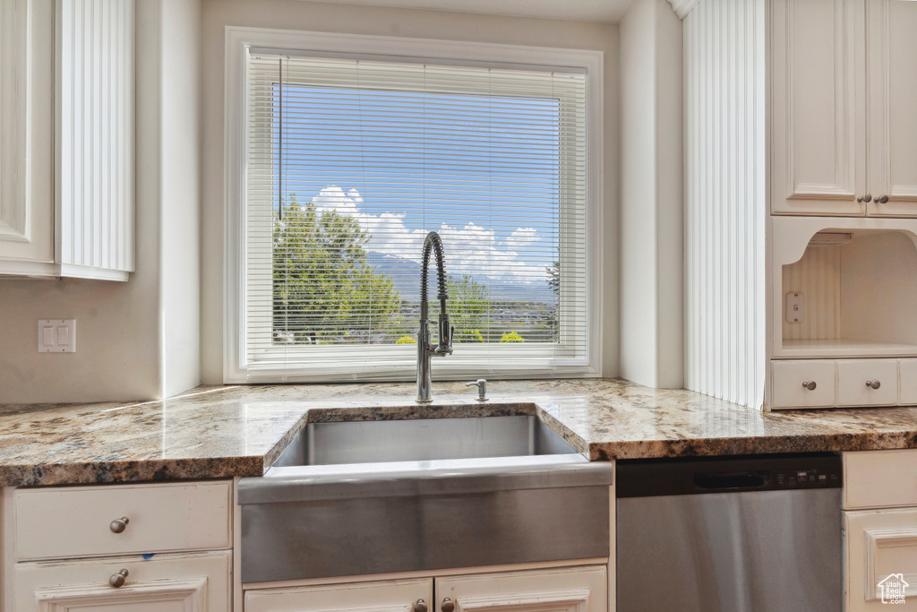 Kitchen featuring white cabinetry, light stone countertops, a sink, and dishwasher