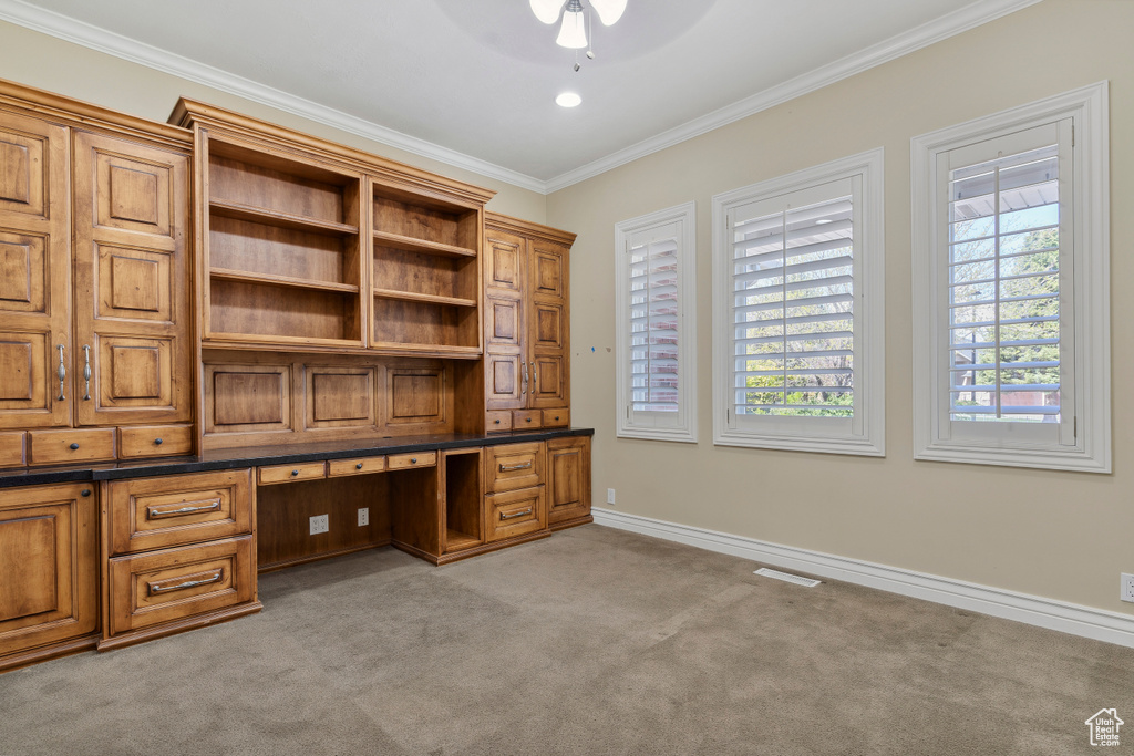 Unfurnished office featuring crown molding, ceiling fan, light carpet, built in study area, and baseboards