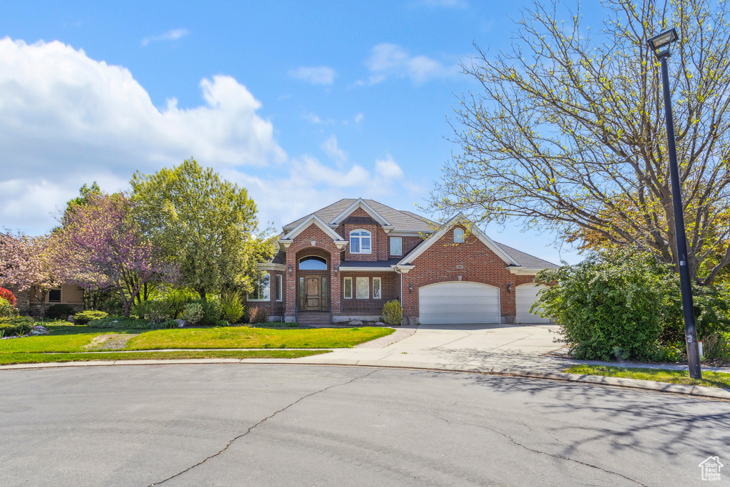 Traditional-style house featuring a garage, concrete driveway, a front lawn, and brick siding