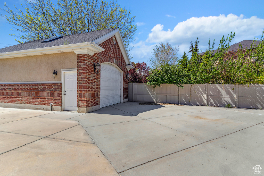 View of side of property with brick siding, driveway, fence, and a garage