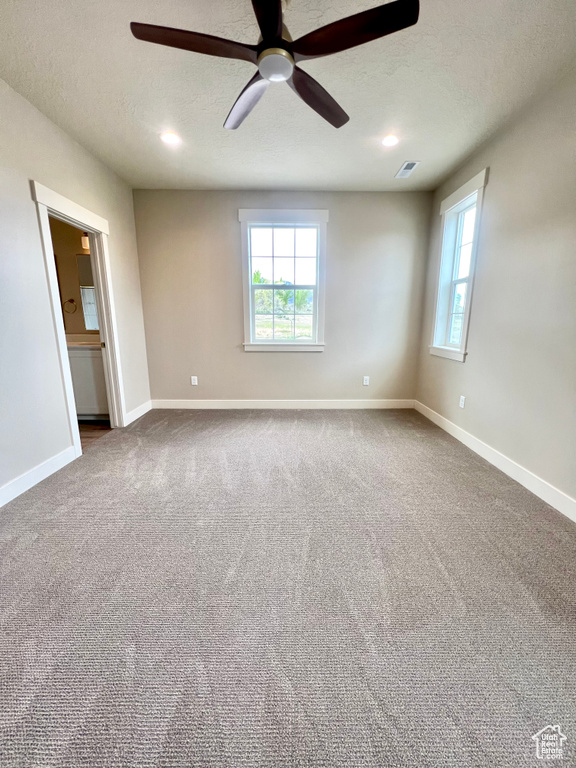 Unfurnished room featuring ceiling fan, visible vents, a healthy amount of sunlight, and dark carpet